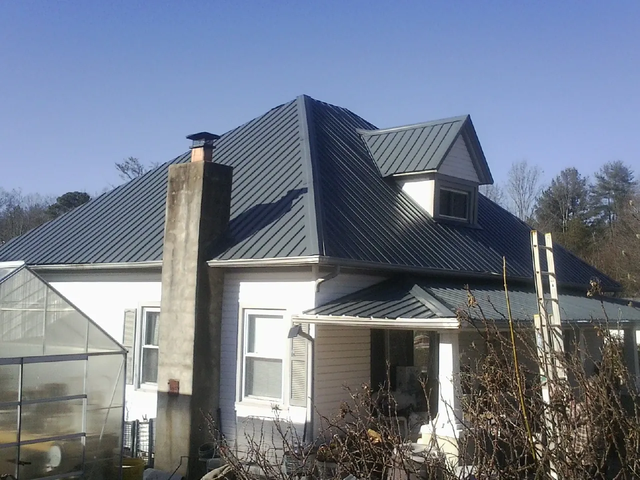 Dark blue standing seam metal roof on a white farmhouse with dormer — Slate & Tile Roof Repair by Roofing Brothers in Lincolndale