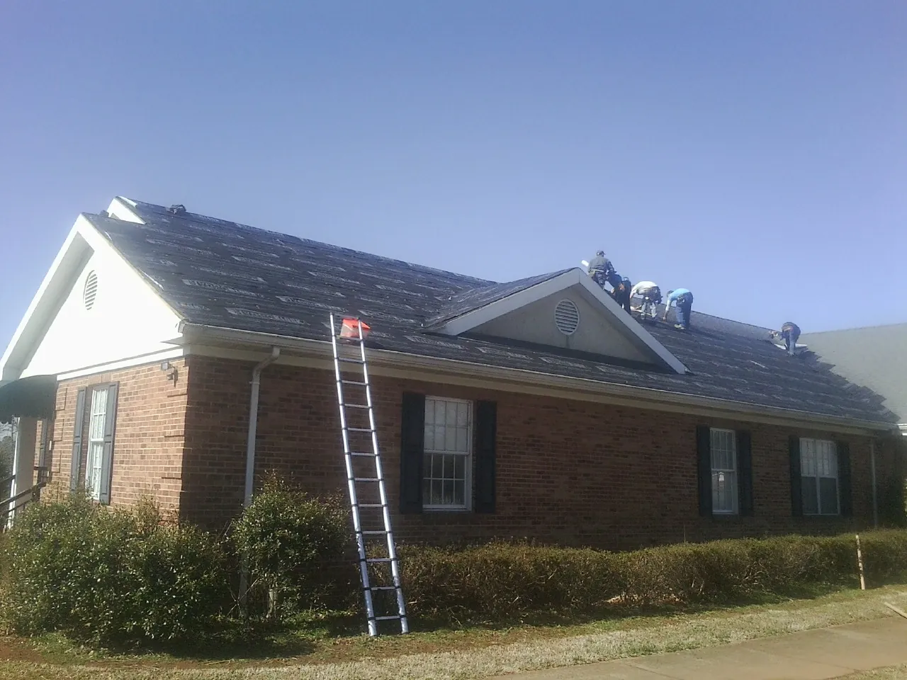 Crew tearing shingles off a brick ranch roof with a ladder set — Emergency Roof Repair work by our crew in Lincolndale