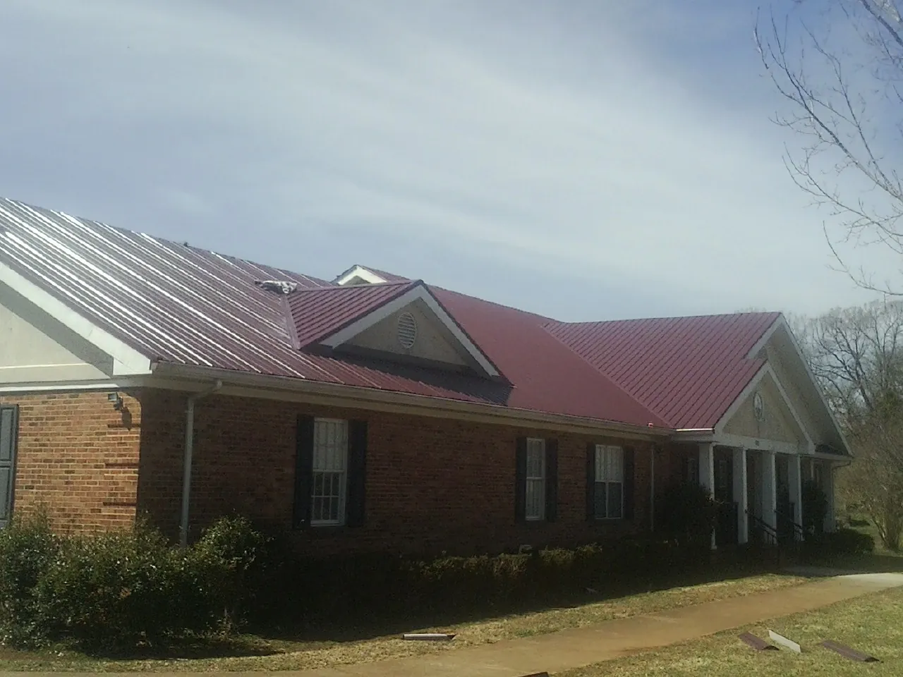 Red metal roof with gabled entries on a long brick building, from a Hail Damage Roof Repair job in Lincolndale