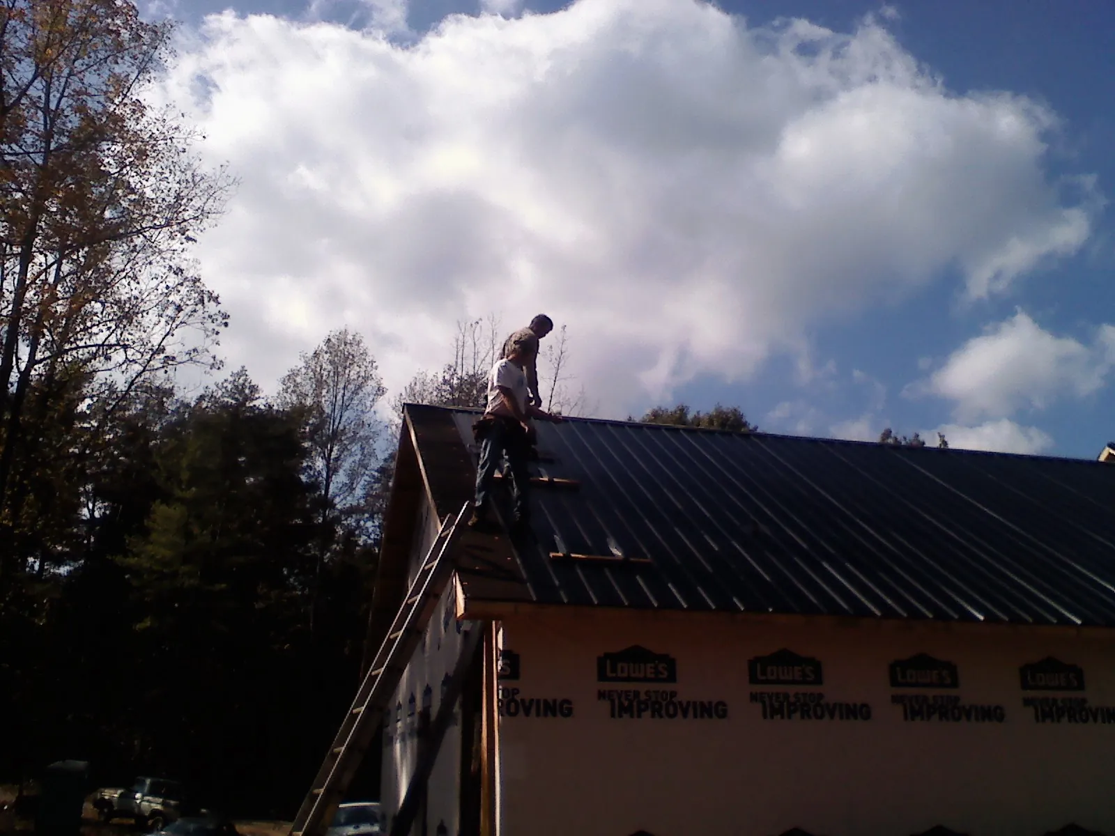Roofer fastening dark metal panels high against a cloudy sky, from a Roof Inspection job in Lincolndale