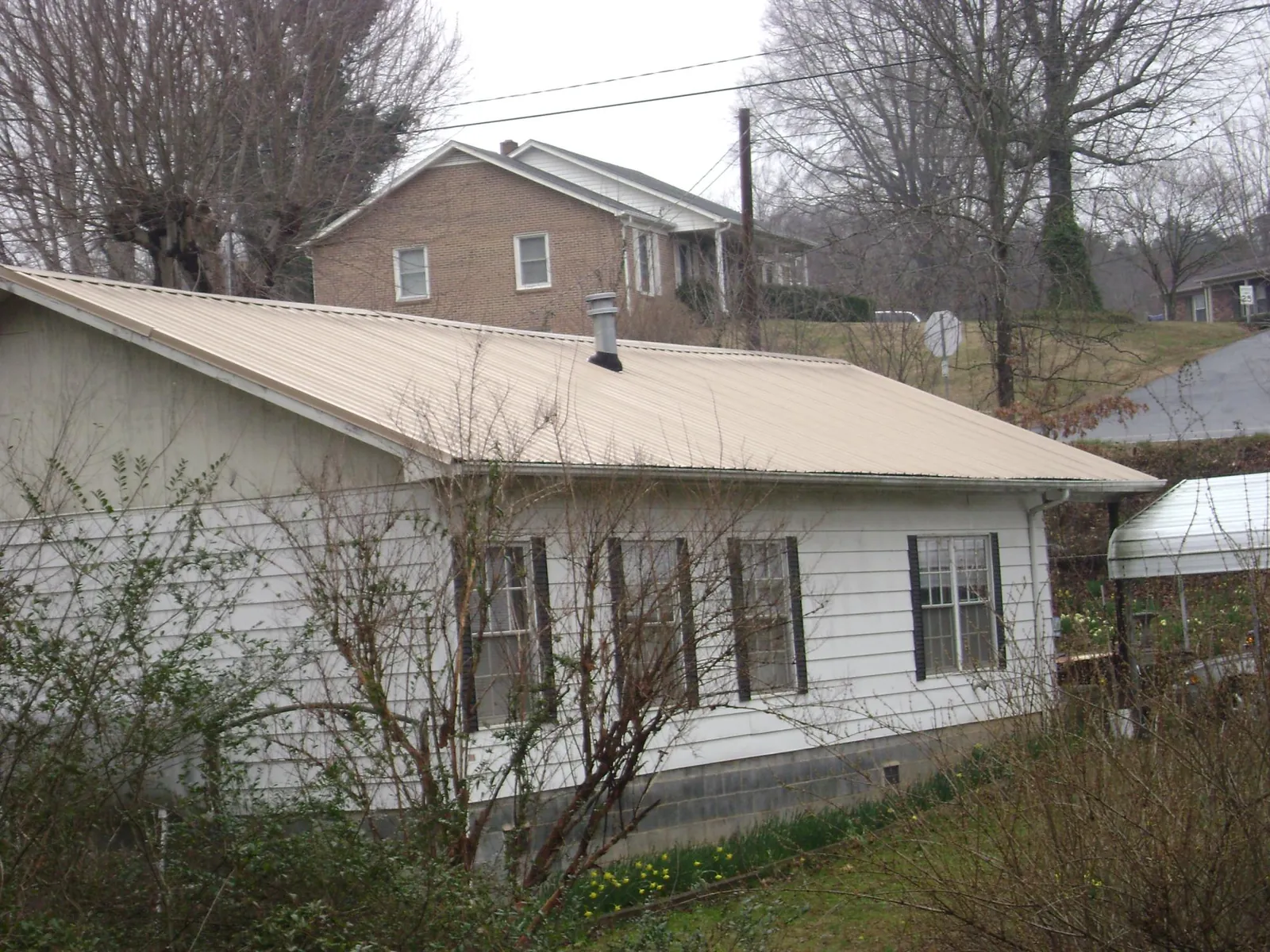 Tan metal roof on a white sided house set into a hillside — Commercial Roofing by Roofing Brothers in Lincolndale
