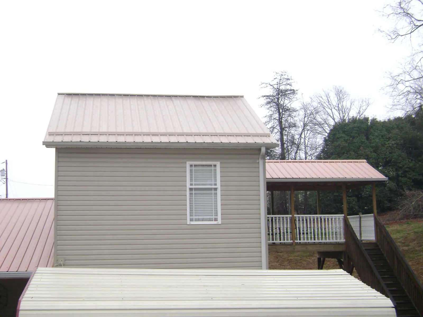 Tan metal roofs on a two story addition and attached porch, from a Roof Replacement job in Lincolndale